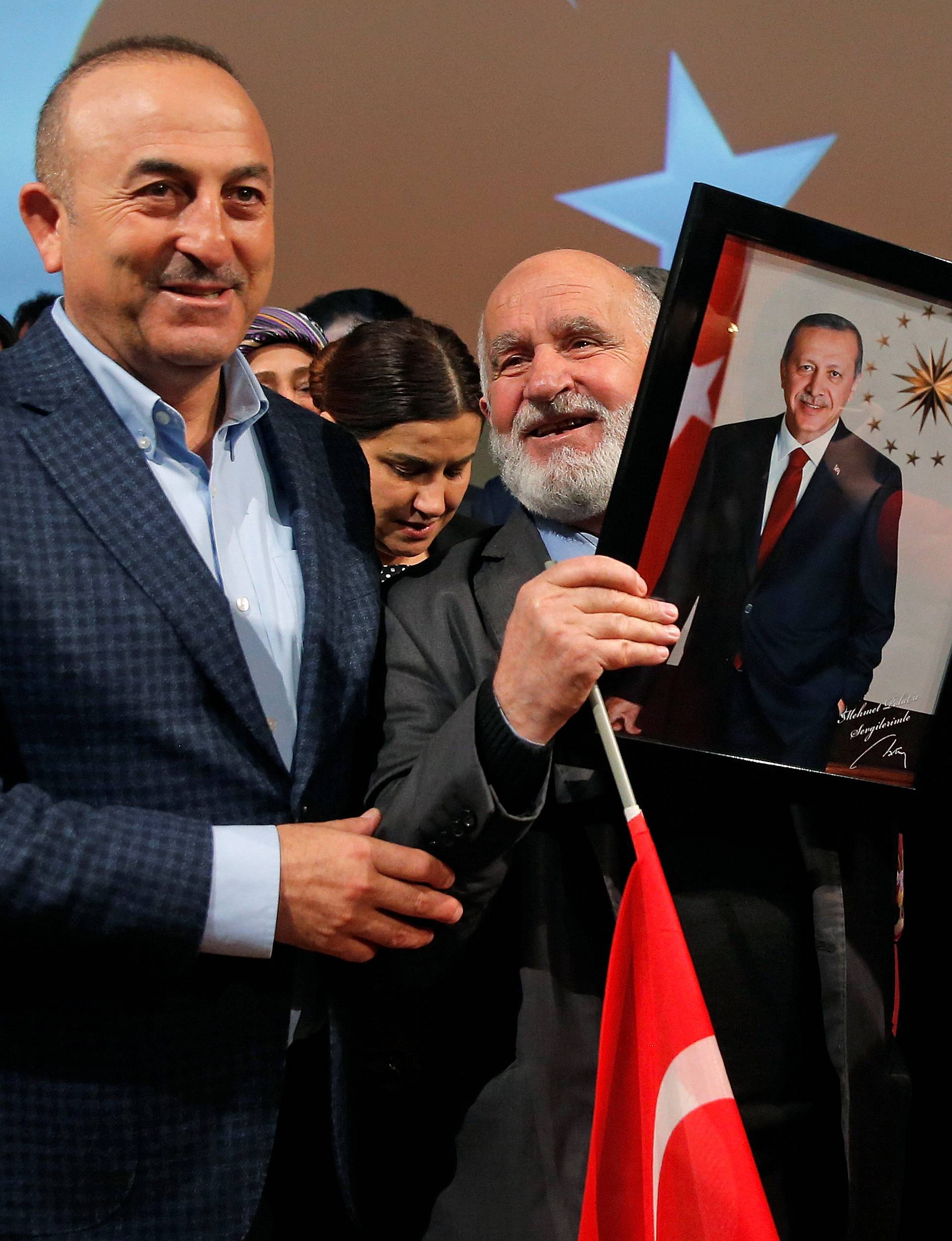 Turkish Foreign Minister Cavusoglu poses with a supporter holding portraits of Turkish President Erdogan and Prime Minister Yildirim at the end of a political rally on Turkey's upcoming referendum, in Metz