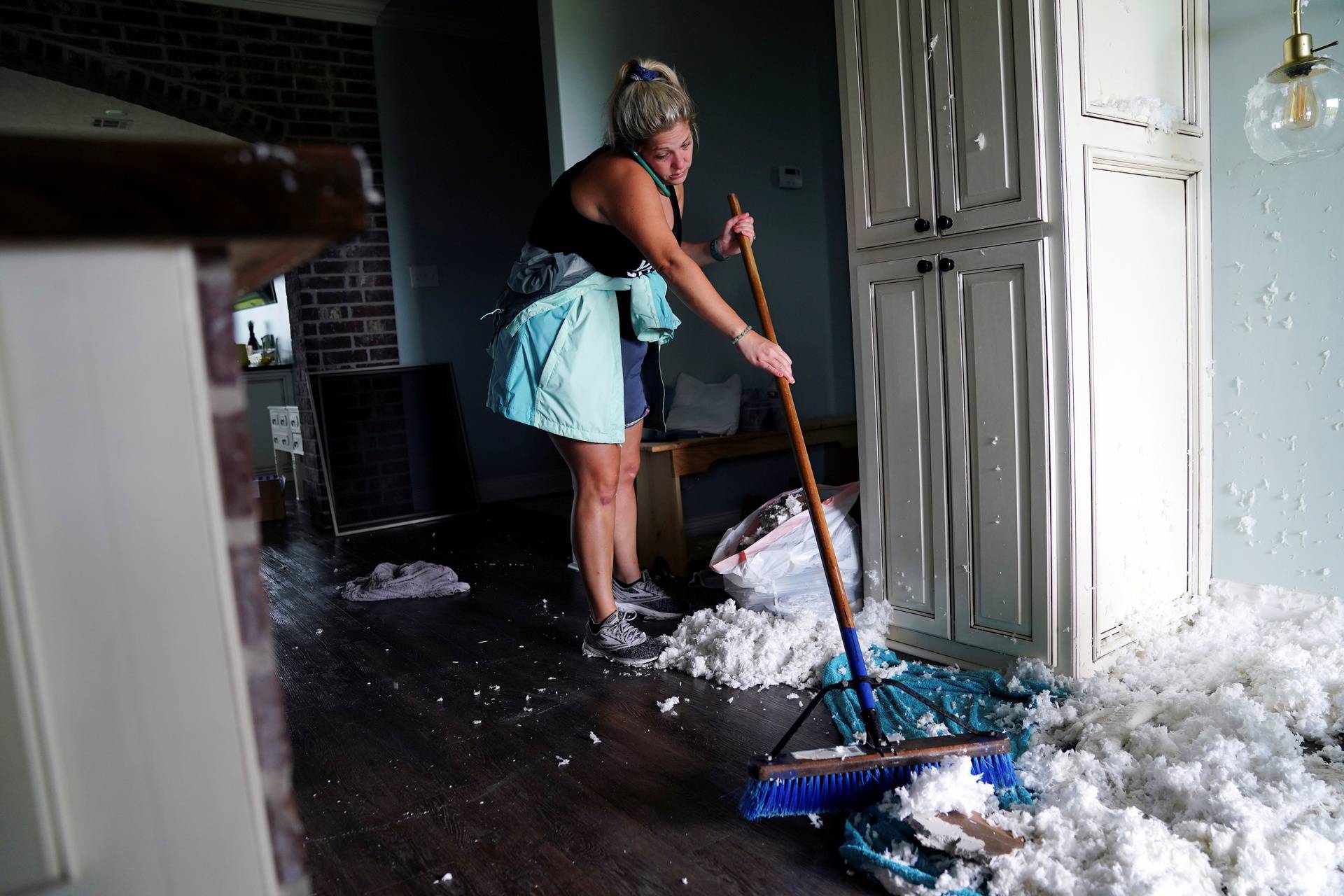 Jade Kingham cleans up ceiling insulation from her kitchen floor after Hurricane Laura passed through the area in Cameron Parish