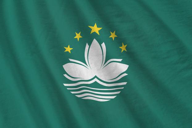 Macau flag with big folds waving close up under the studio light indoors. The official symbols and colors in banner