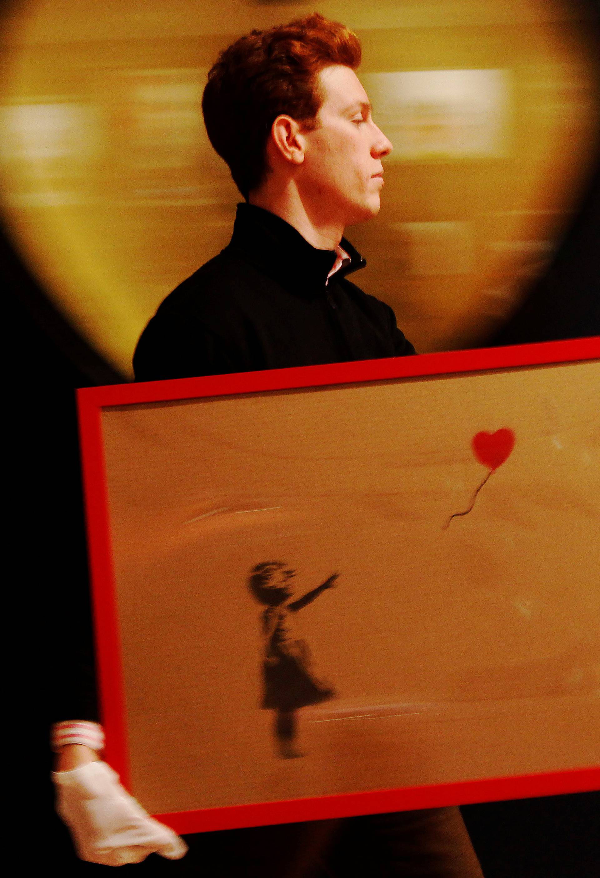 FILE PHOTO: An employee walks with artist Banksy's "Girl and Balloon" 2009 signed and inscribed For Mike, past artist  Ryan Callanan's (known as RYCA) "Mega Heart" 2011 at Bonhams auction house in London