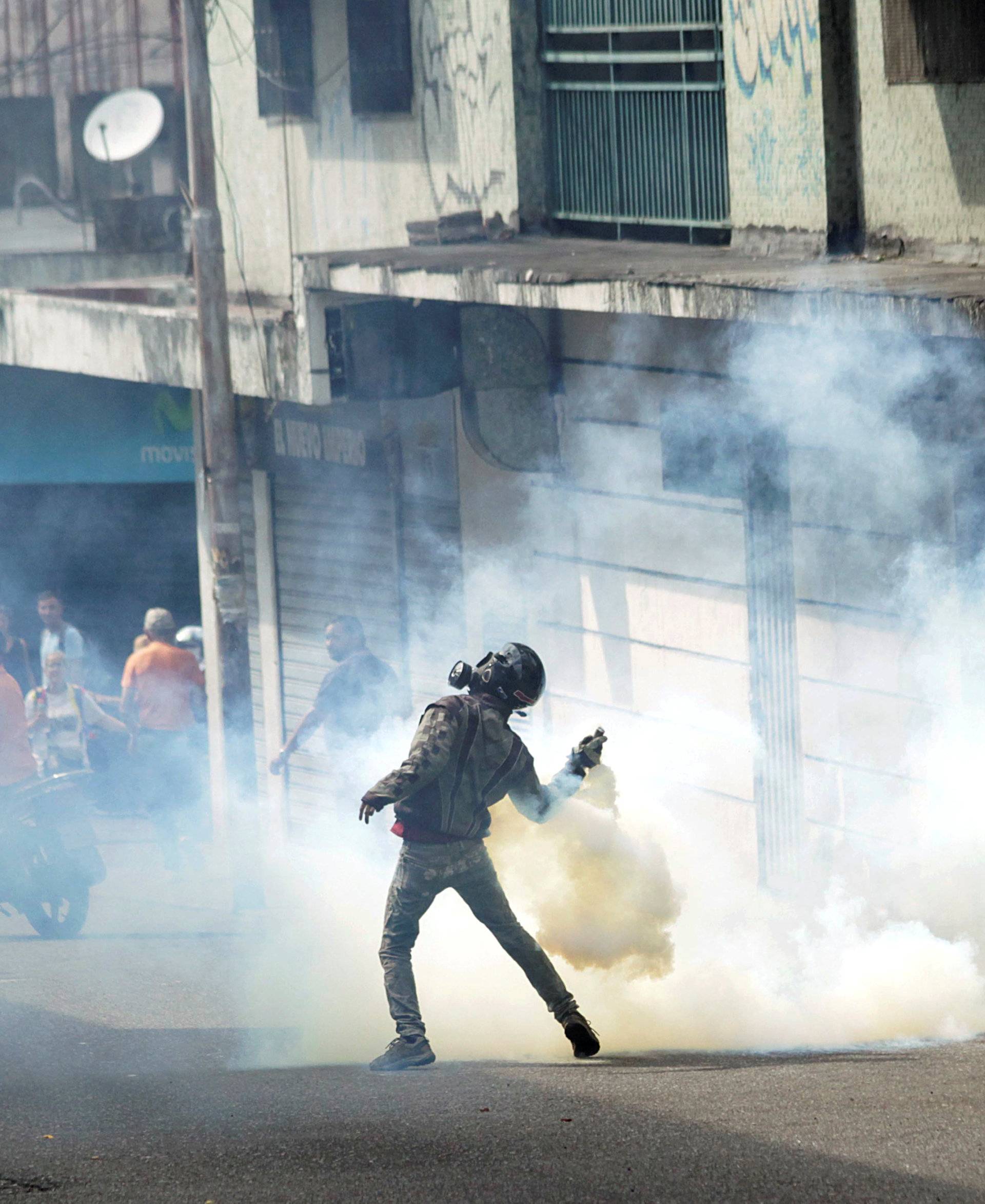 A demonstrator throws back a gas canister while clashing with security forces during a rally in Tachira