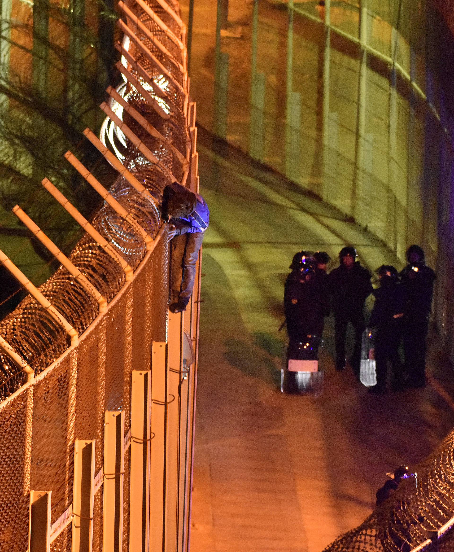 An African migrant stands on top of a border fence as Spanish police stand guard below during a failed attempt to cross into Spanish territories between Morocco and Spain's north African enclave of Ceuta