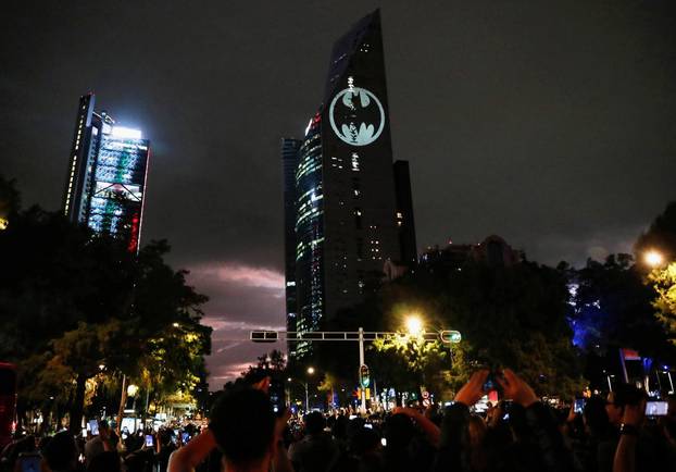People take pictures of a Bat-Signal projected onto a building at night as Batman fans celebrate the 80th anniversary of the first appearance of the DC Comics superhero, in Mexico City