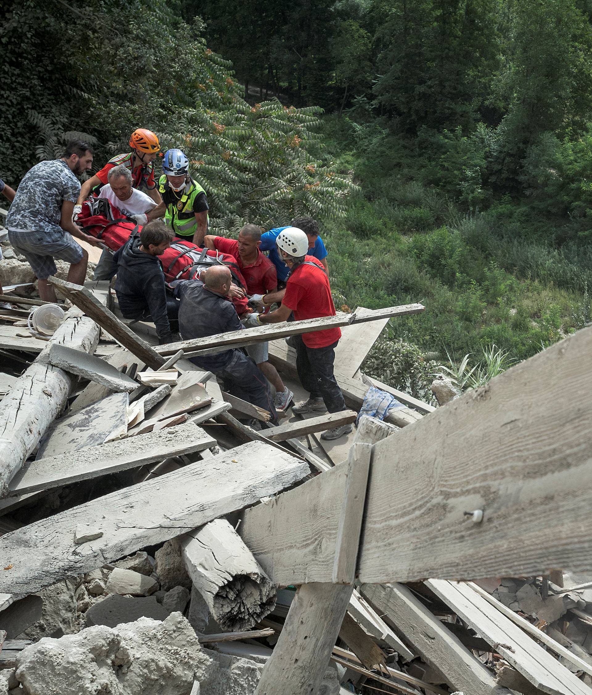 A wounded person is carried out from rubble in front of a collapsed building following an earthquake in Pescara del Tronto