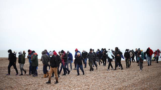 Migrants walk along a beach after being brought ashore by a RNLI Lifeboat, after having crossed the channel, in Dungeness