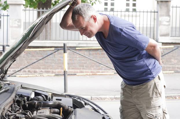 A  man having a bad day checks under the hood of his car to figu