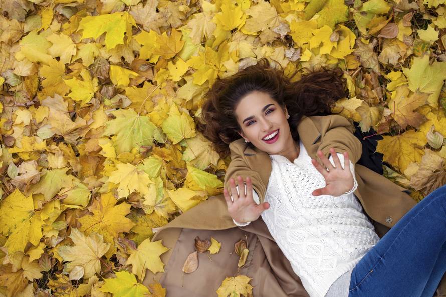 Young beautiful girl in blue jeans lying on yellow leaves