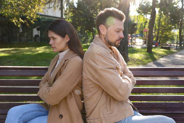 Upset arguing couple sitting on bench in park. Relationship prob