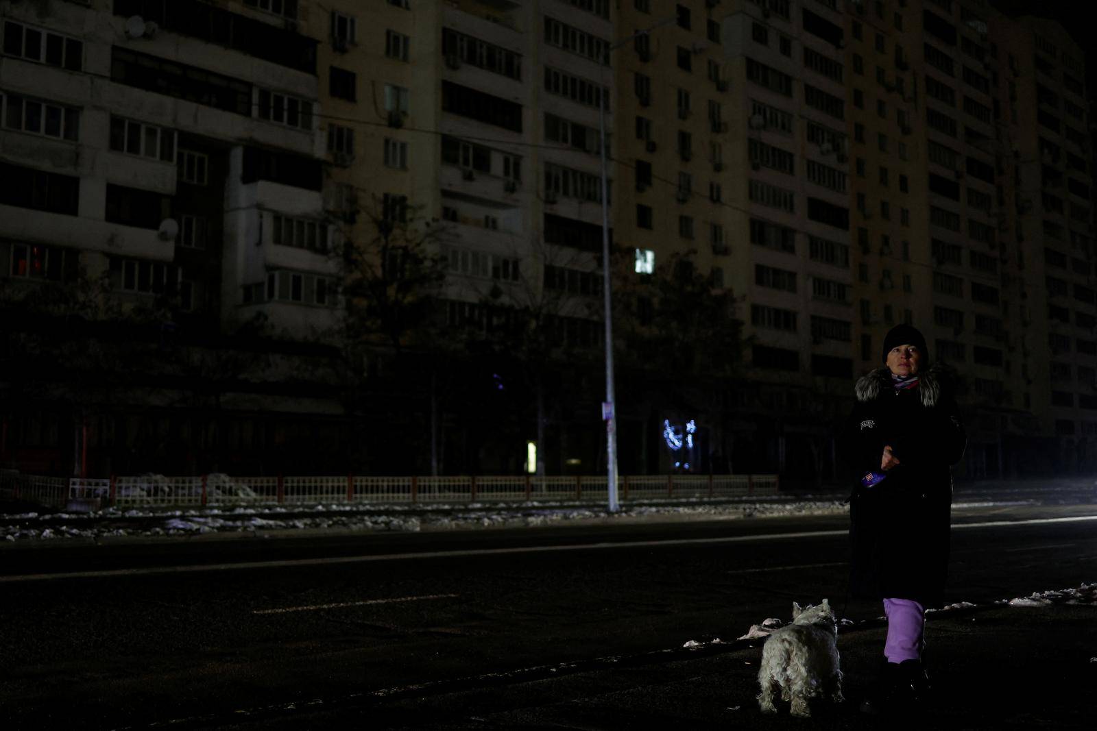 Woman with a dog waits for a bus in a street without electricity after critical civil infrastructure was hit by Russian missile attacks in Kyiv