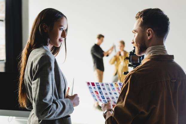 selective focus of producer with photographer talking on backstage and hairstylist with model on background