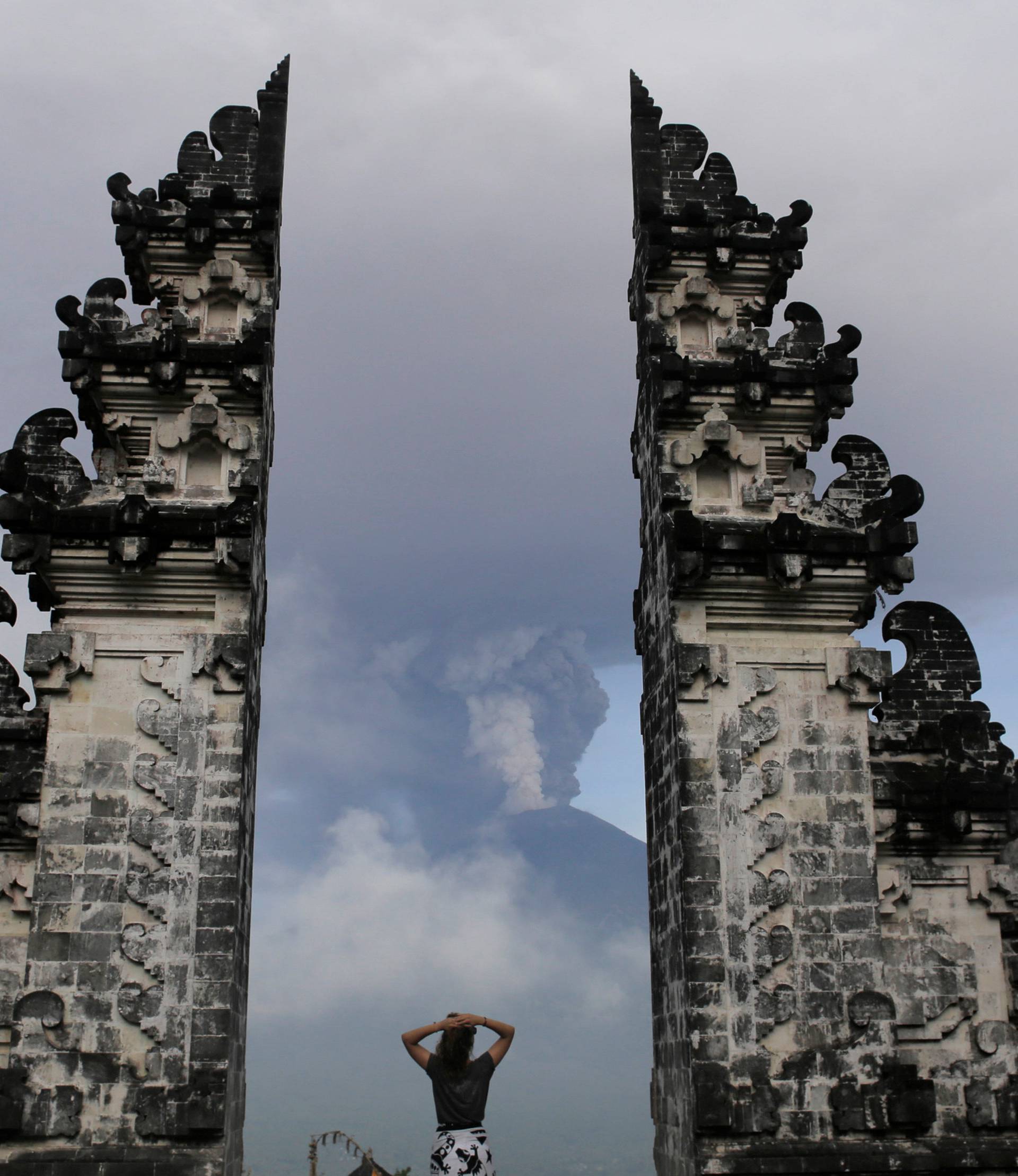 A tourist watches as Mount Agung volcano erupts at Lempuyang Temple in Karangasem, Bali