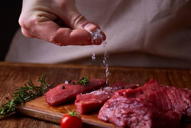 Strong professional man's hands spilling salt on raw beefsteak, selective focus, close-up