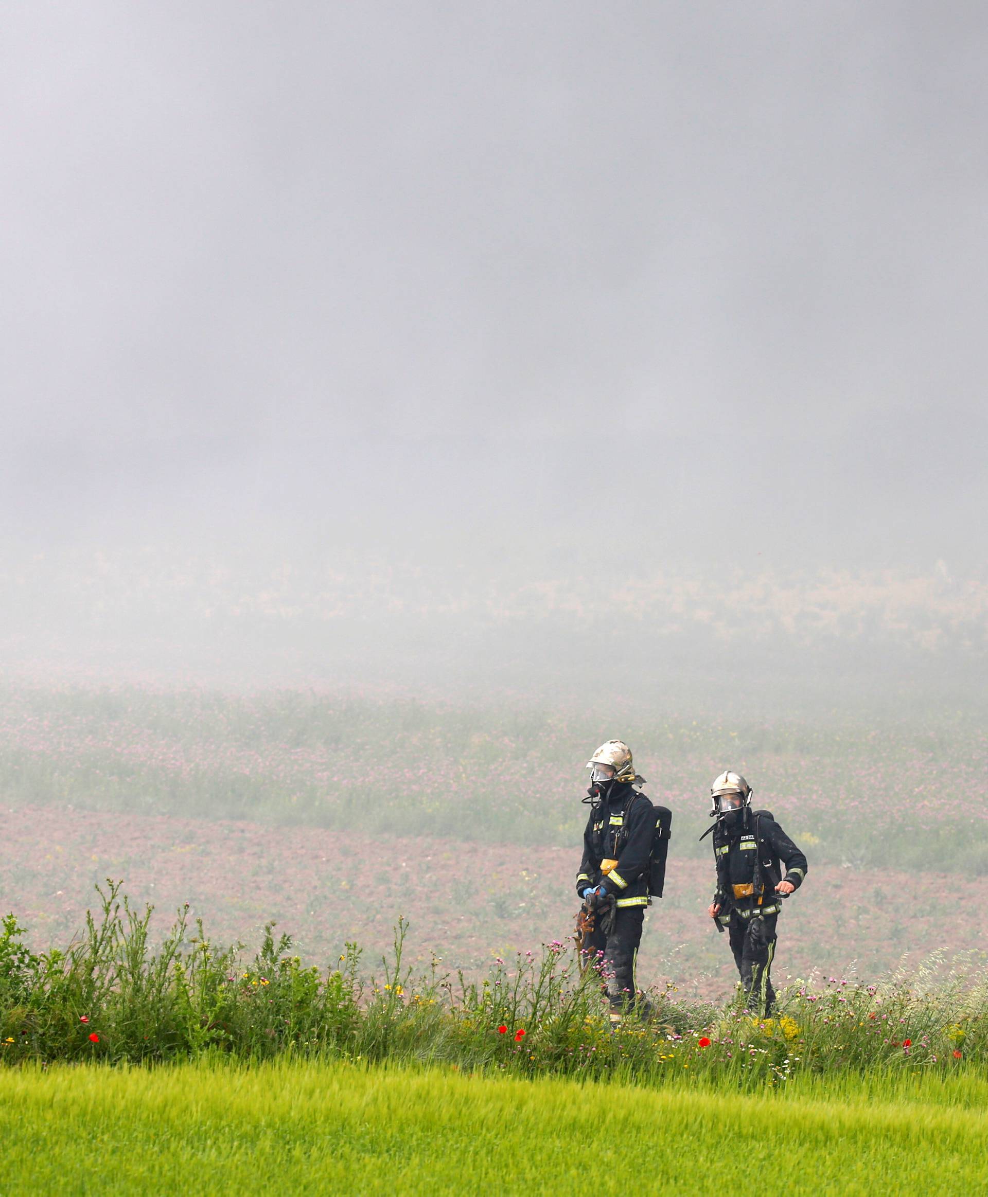 Firefigthers walk amidst smoke during a fire at a tire dump near a residential development in Sesena