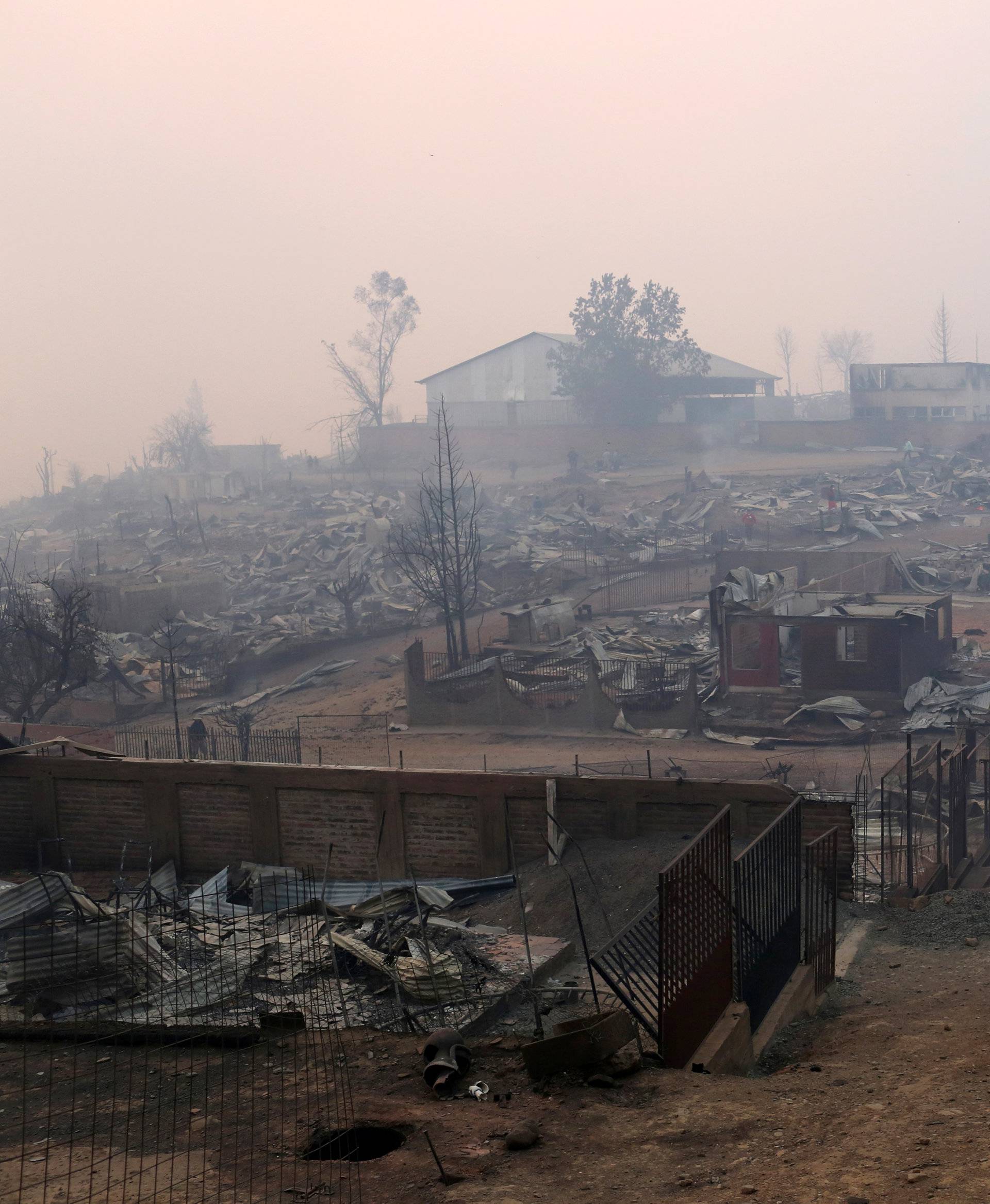People hug while standing next to burnt houses as the worst wildfires in Chile's modern history ravage wide swaths of the country's central-south regions, in Santa Olga