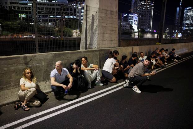 People take cover by the side of a road as a siren sounds, after Iran fired a salvo of ballistic missiles at Israel, in Tel Aviv