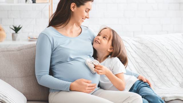 Little daughter putting baby little boots on expecting mother tummy