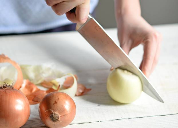 Woman hand cut fresh onion on white table