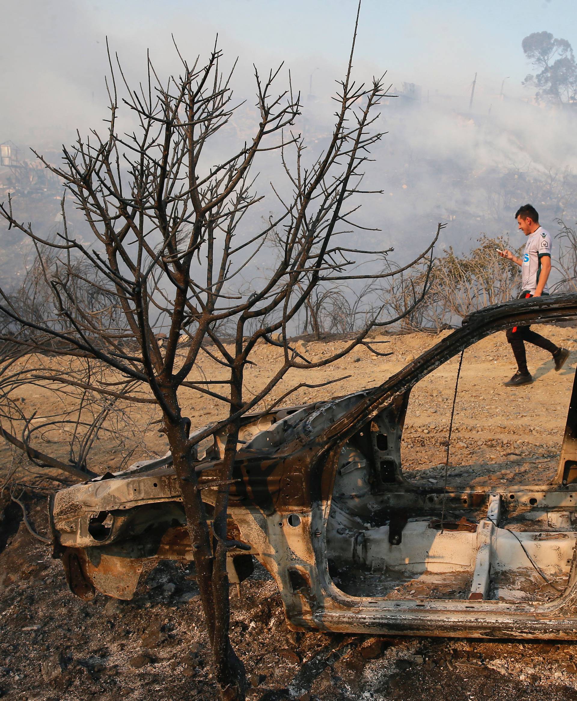 A resident is seen next to a burned car in front of dozens of houses burned on a hill, due to a forest fire but there have been no reports of death, local authorities said in Valparaiso, Chile