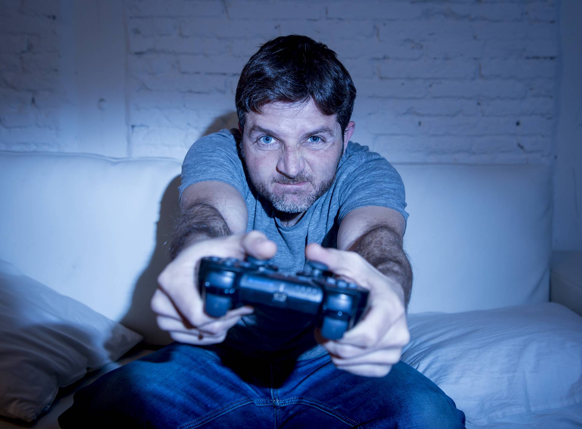 young excited man at home sitting on living room sofa playing video games using remote control joystick