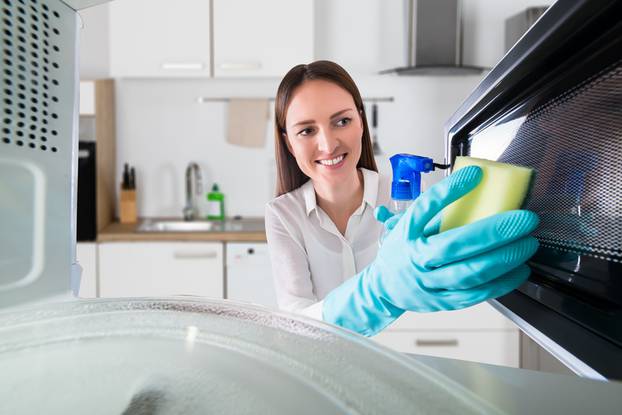 Woman Cleaning Microwave With Spray Bottle And Sponge