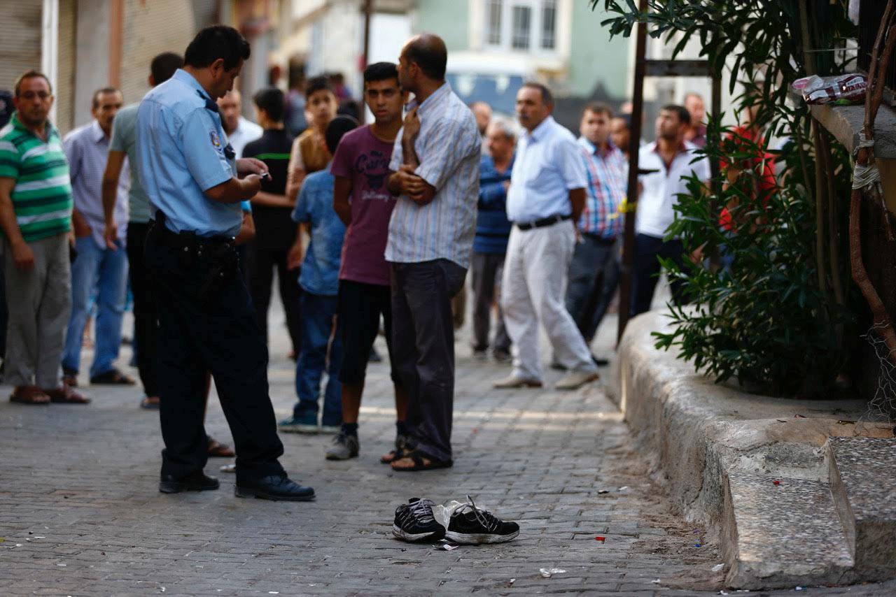 A police officer secures the scene of an explosion as locals stand next to him after a suspected suicide bomber targeted a wedding celebration in the Turkish city of Gaziantep