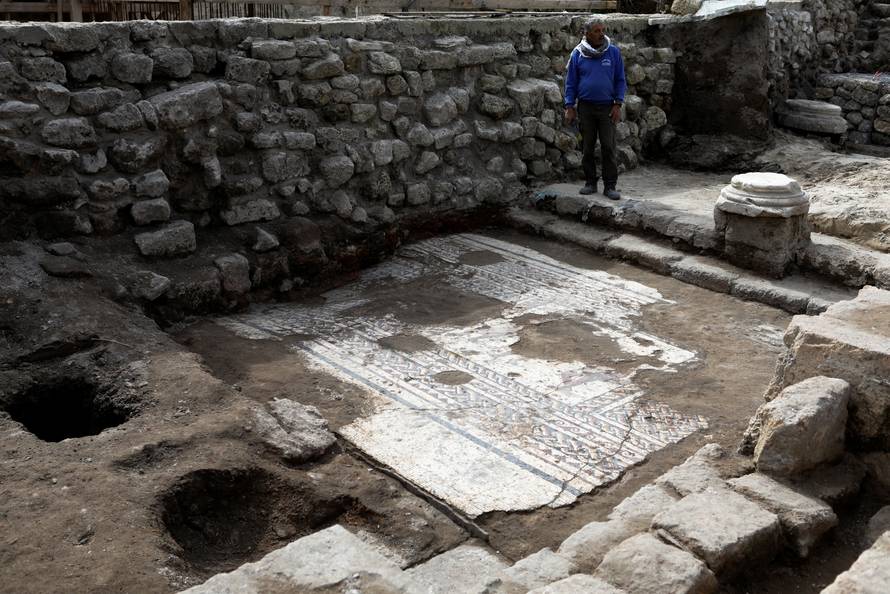 An Israel Antiquities Authority worker stands next to a mosaic floor which archaeologists say is 1,800 years old and was unearthed during an excavation in Caesarea