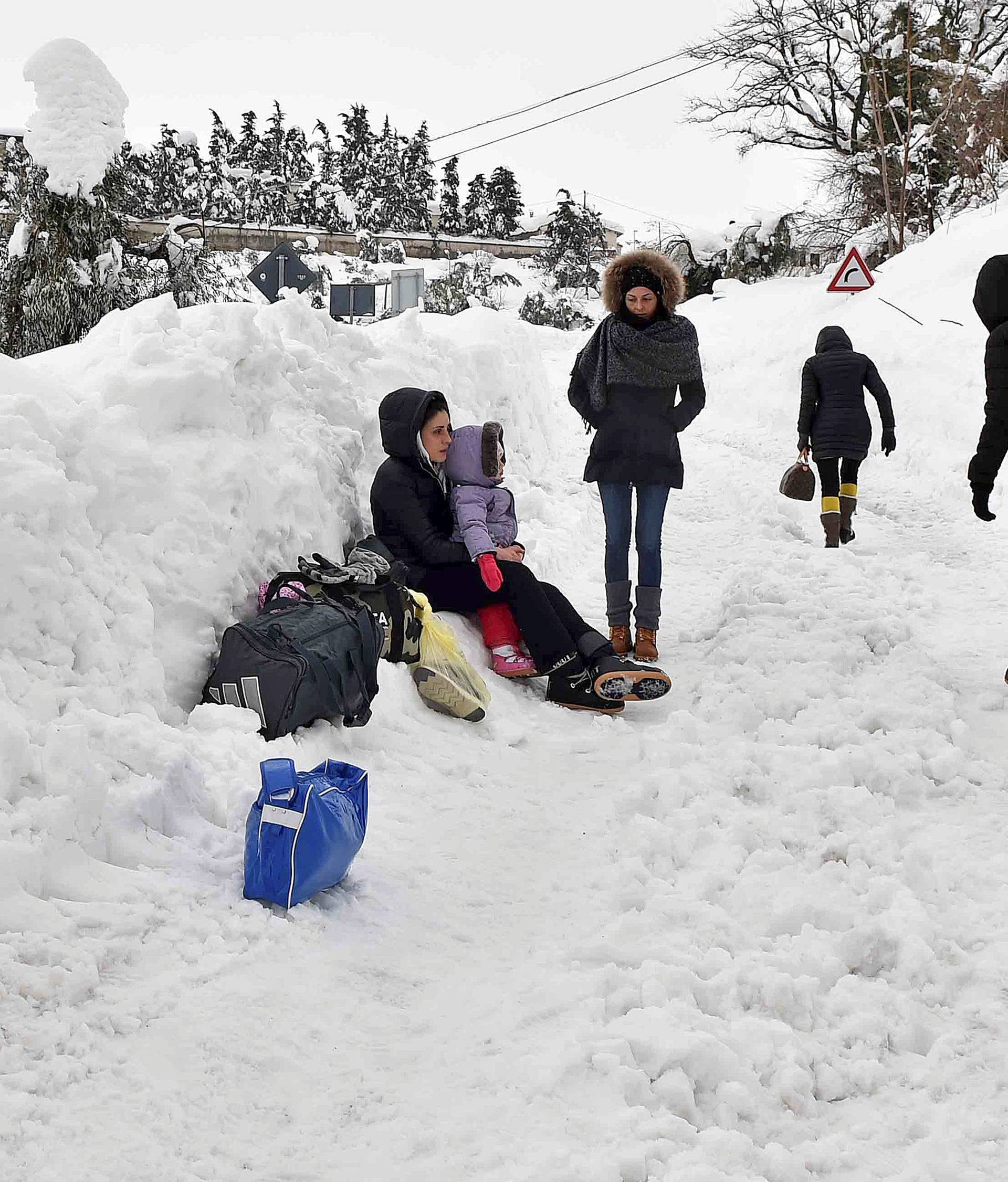 People stand with their luggage in the town of Penne, central Italy, following a series of earthquakes and a snow avalanche hitting a hotel in central Italy