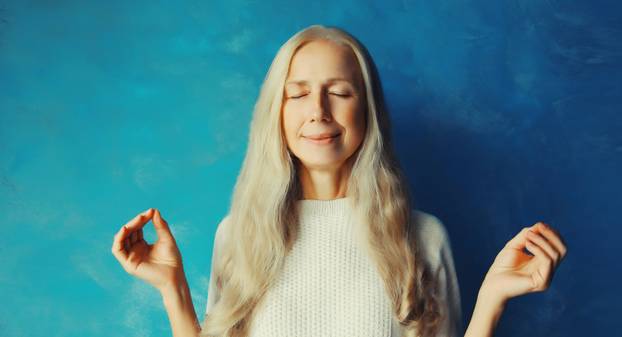 Calm relaxed healthy mature woman meditates, practicing doing yoga exercises, stress relief