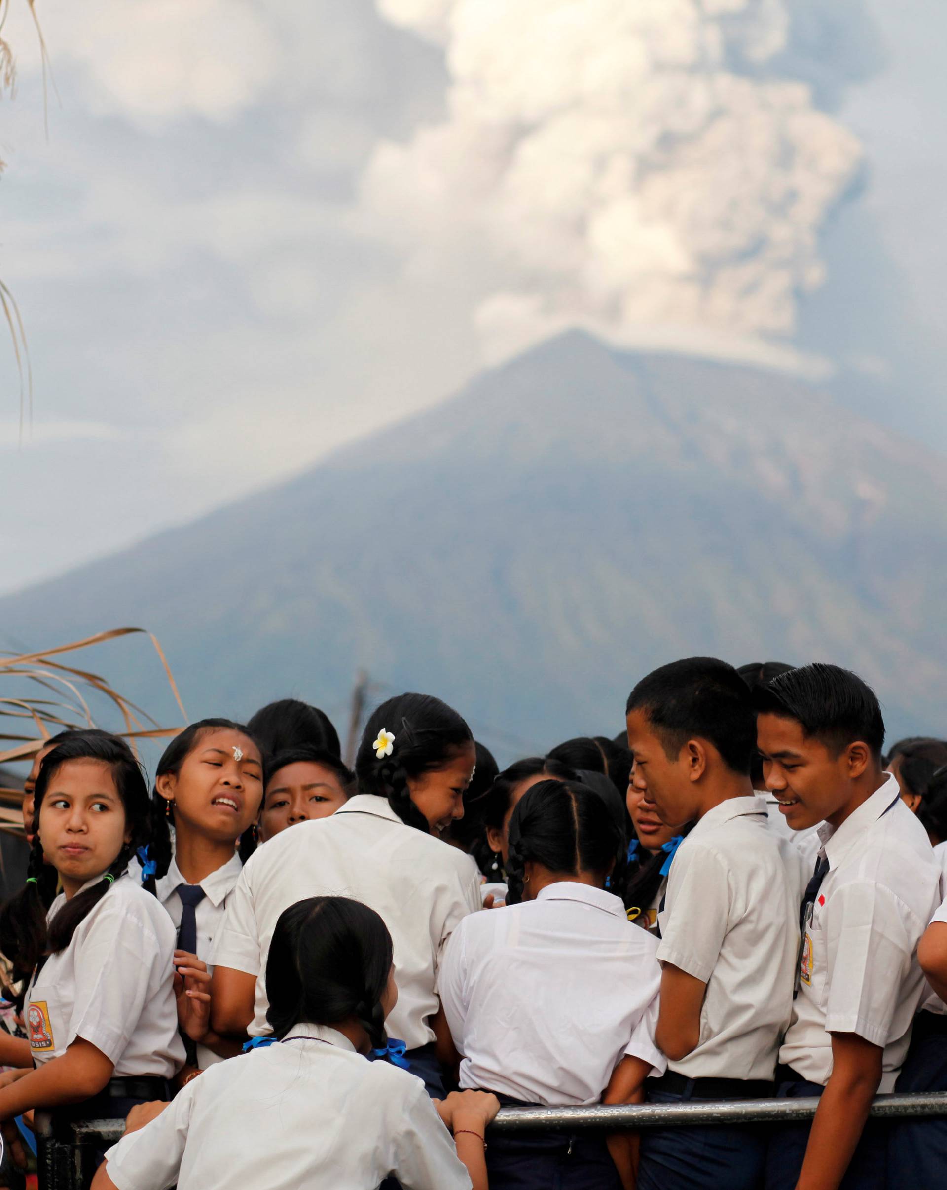 School children ride on the back of a truck on their way to school as Mount Agung volcano erupts in the background near Amed, Karangasem Regency, Bali