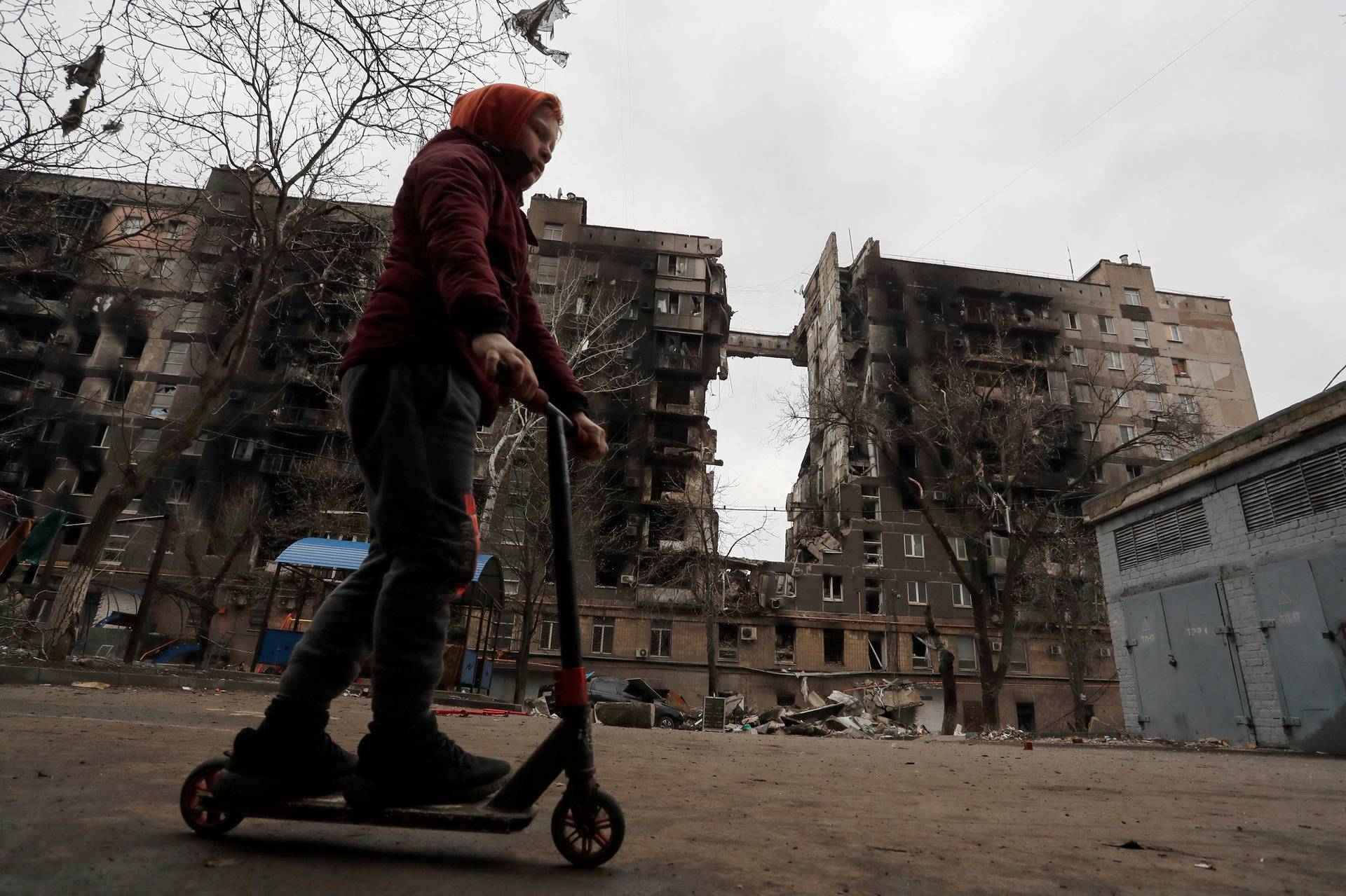 FILE PHOTO: A boy rides a scooter near a destroyed building in Mariupol