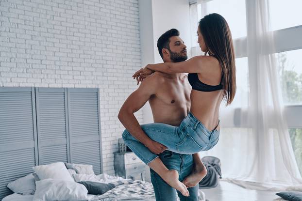 Playful couple. Beautiful young couple embracing while standing face to face in the bedroom