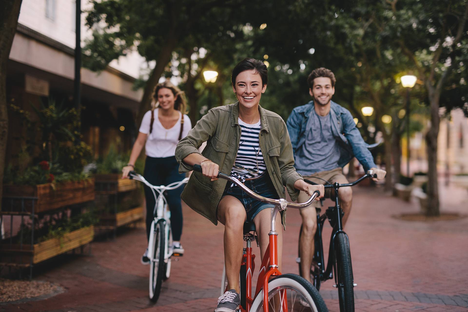Three,Young,People,Cycling,Down,The,Street.,Male,And,Female