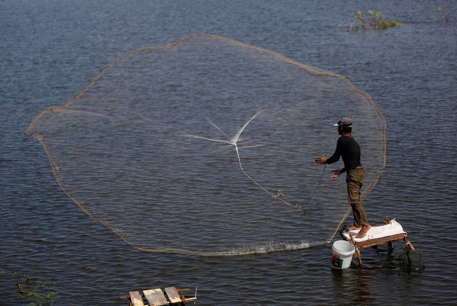 A man casts a fishing net into a lake in Kandal province, Cambodia