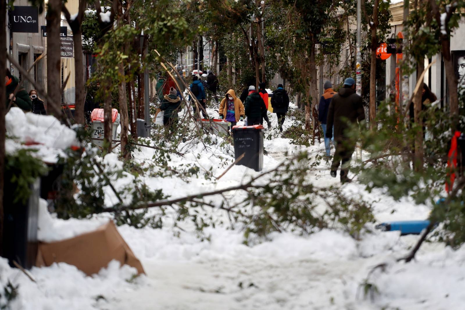 People walk through the snow and among fallen branches in Madrid