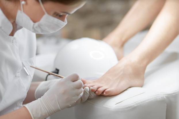 Professional in beauty salon cleaning nails on feet