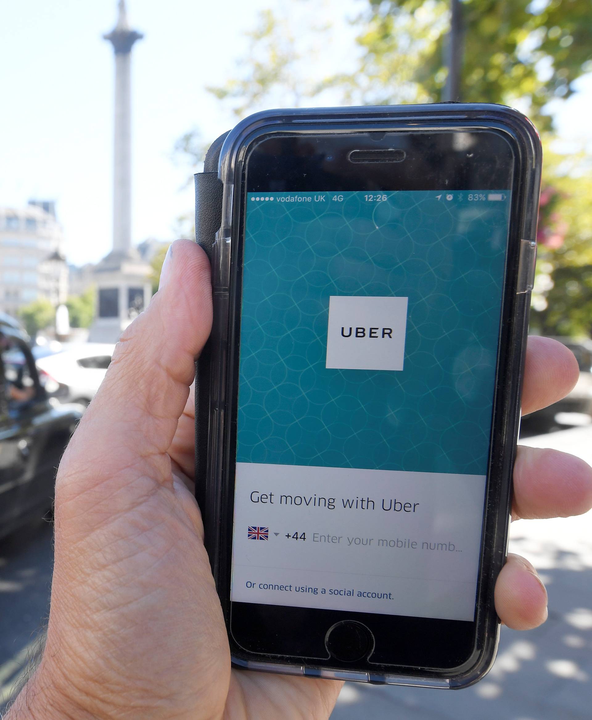 A photo illustration a London taxi passing as the Uber app logo is displayed on a mobile telephone, as it is held up for a posed photograph in central London