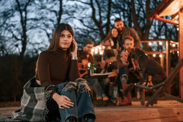 Beautiful young woman is sitting. Group of people is spending time together on the backyard at evening time