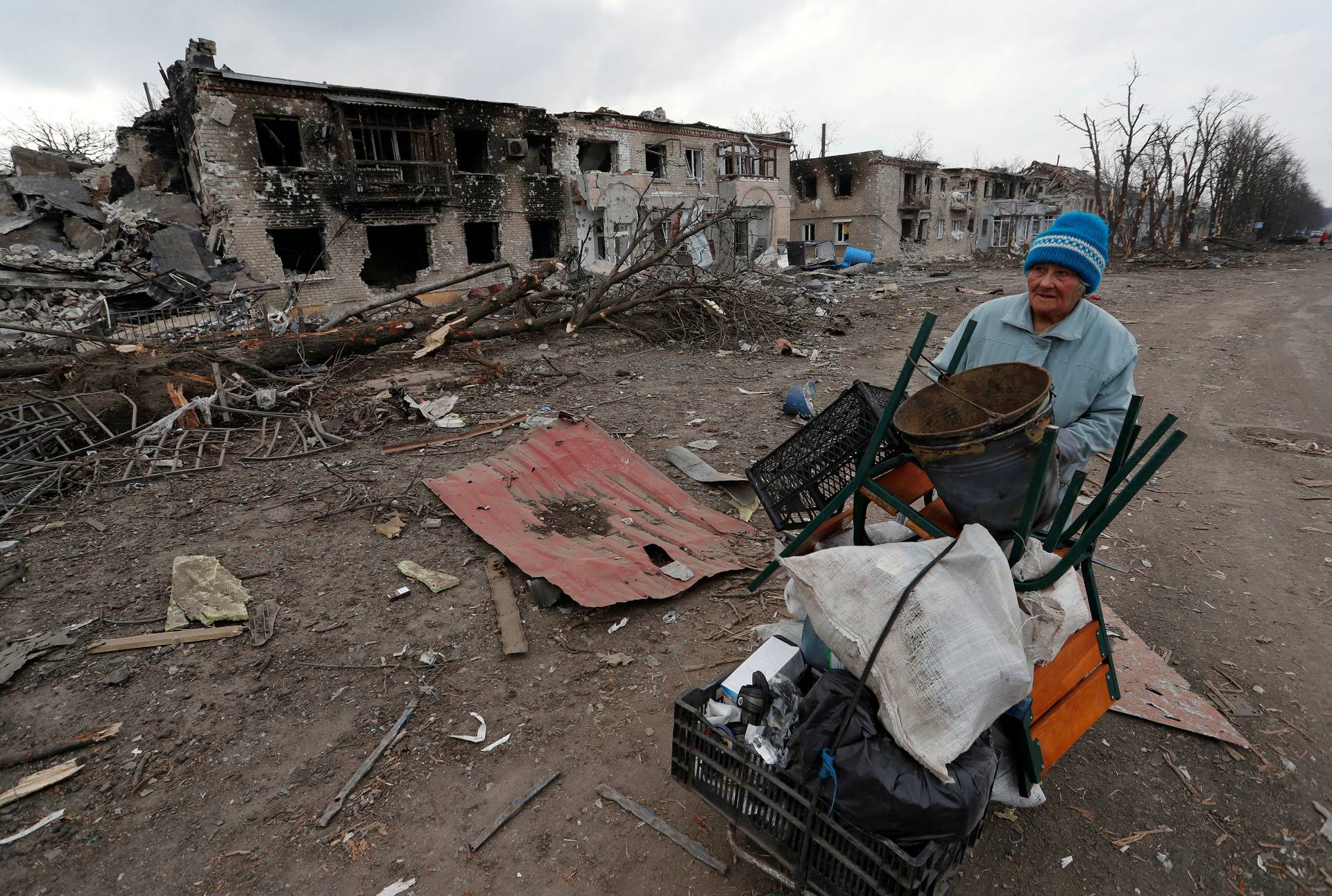 FILE PHOTO: A woman pushes a trolley with her belongings along a damaged street in Volnovakha