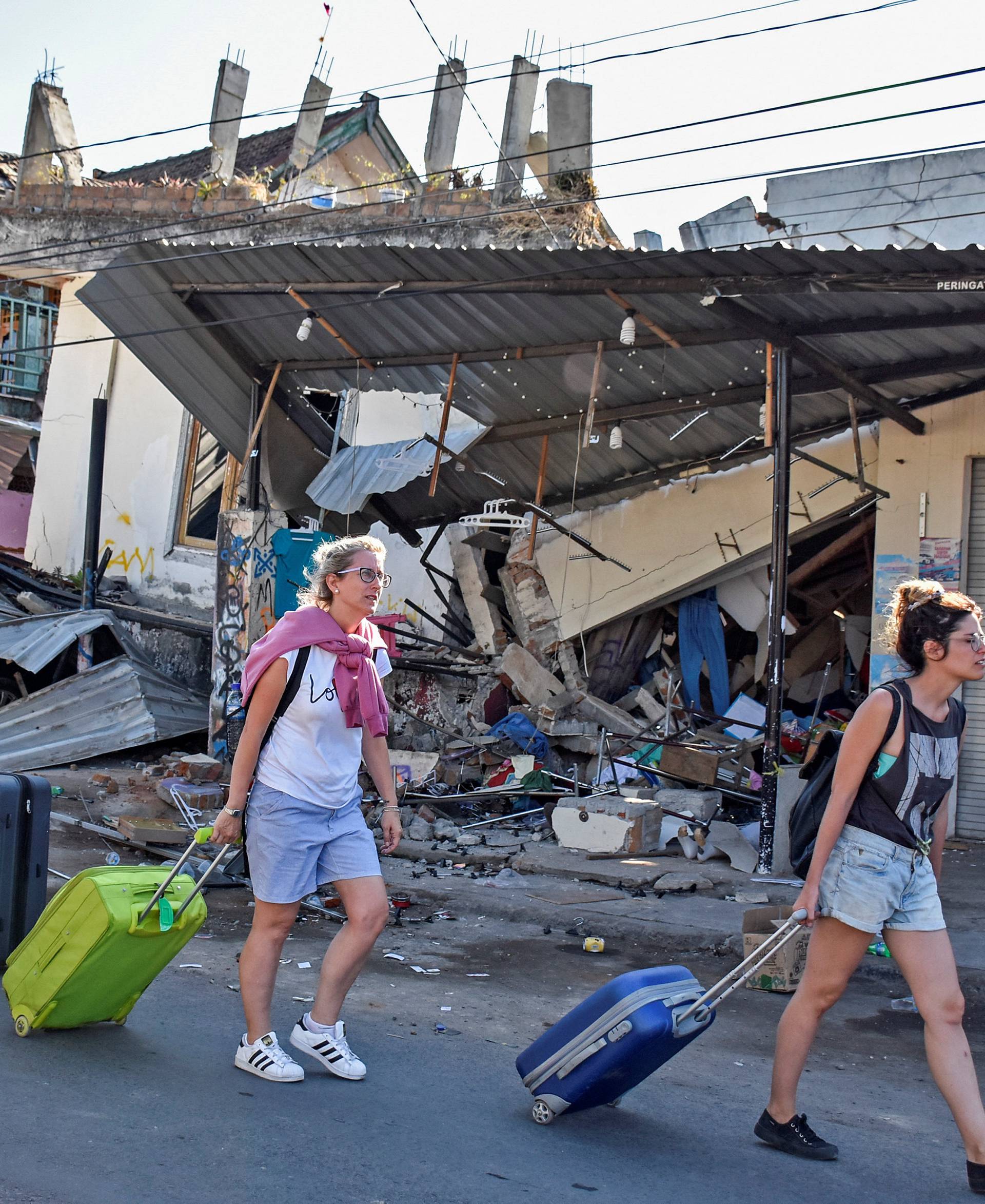 Foreign tourists pull their suitcases as they walk past damaged buildings following a strong earthquake in Pemenang, North Lombok,