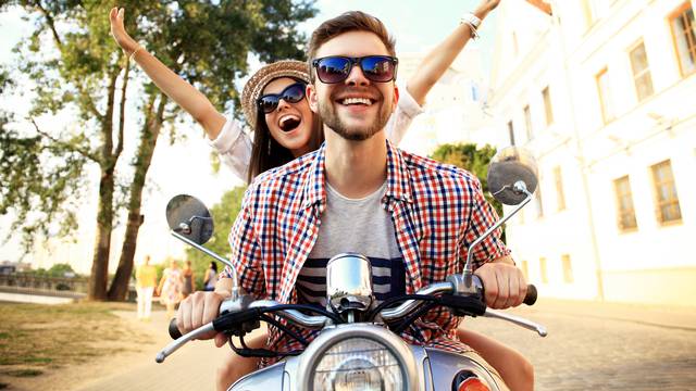 Portrait of happy young couple on scooter enjoying road trip