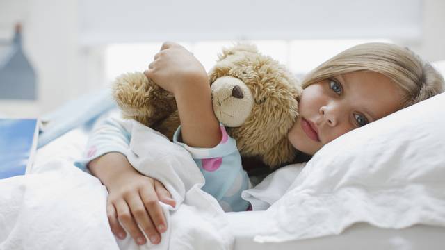 Sick girl laying in bed with teddy bear