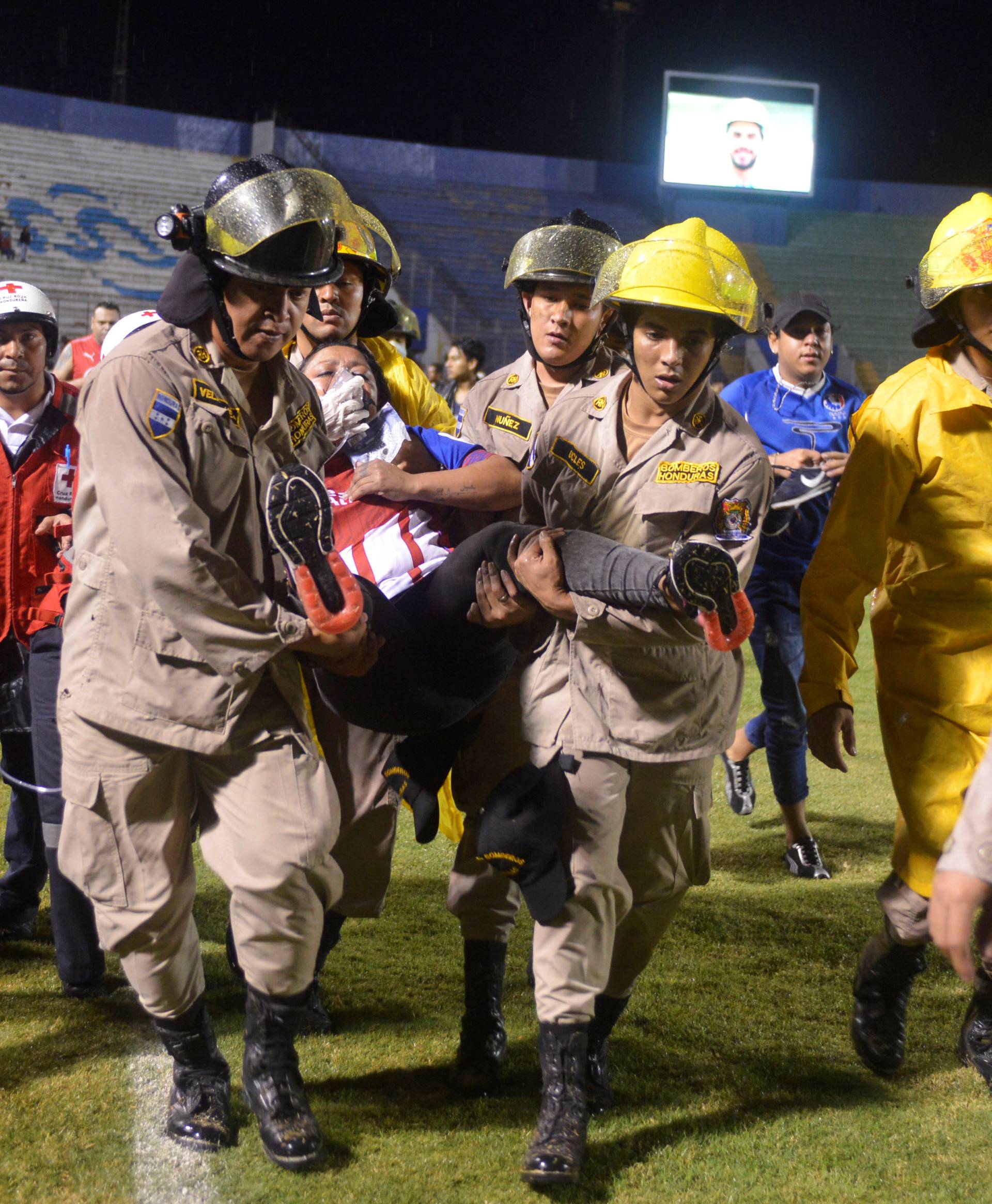 Firefighters carry a woman after three people died in riots before a soccer match when the fans attacked a bus carrying one of the teams, at the National Stadium in Tegucigalpa