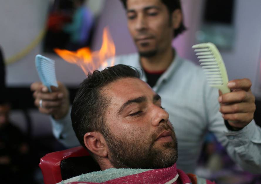 Palestinian barber Ramadan Odwan styles and straightens the hair of a customer with fire at his salon in Rafah, in the southern Gaza Strip