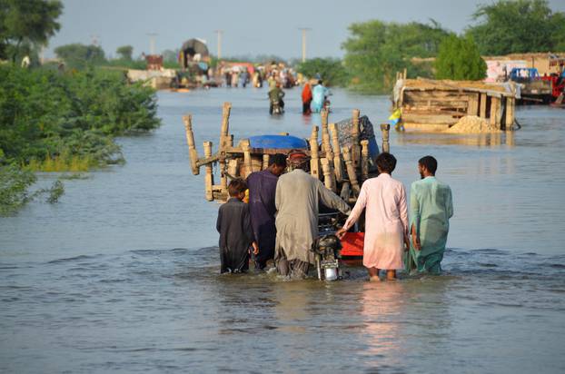 Men walk along a flooded road with their belongings, following rains and floods during the monsoon season in Suhbatpur