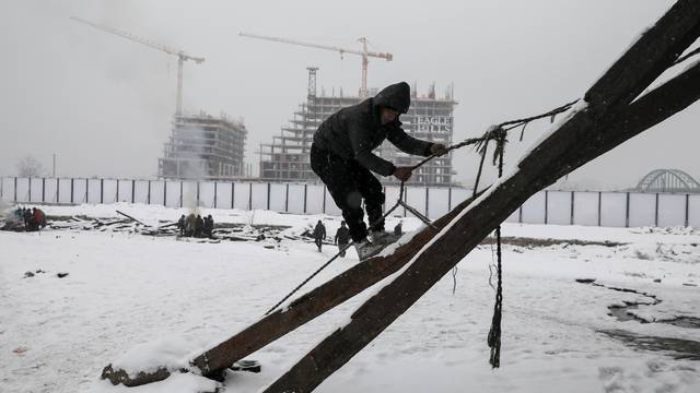 A migrant climbs during a snowfall outside a derelict customs warehouse in Belgrade