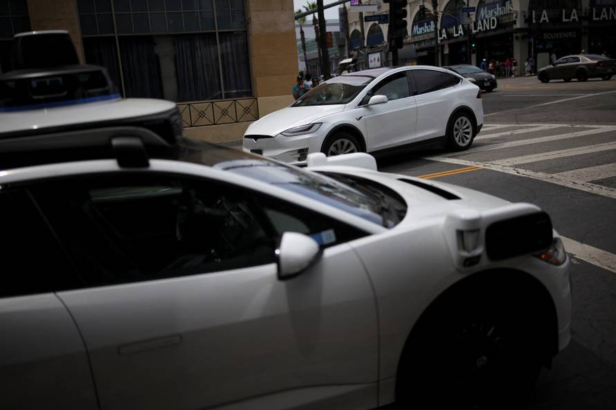 A Tesla drives by a Waymo self-driving car in Los Angeles