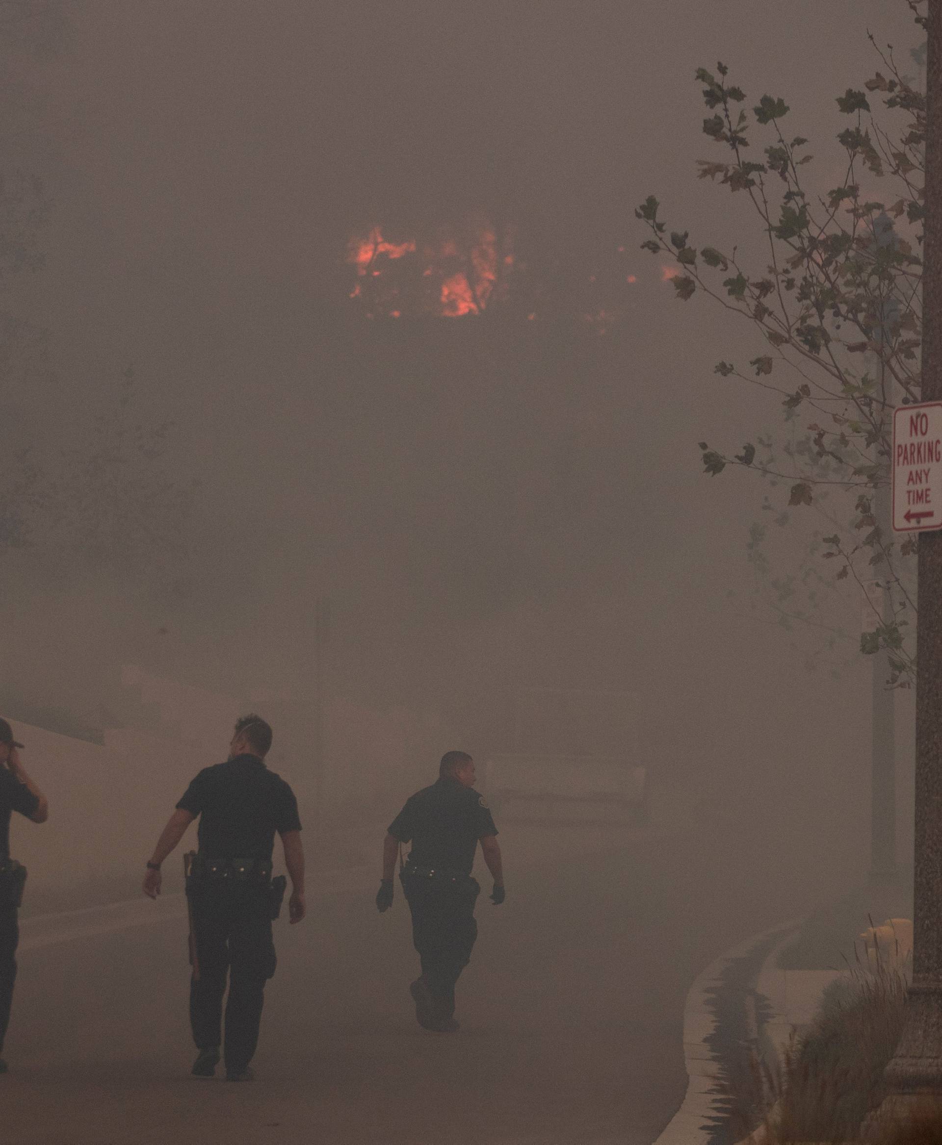 FILE PHOTO: Ventura policemen rush to check a home in a burning neighborhood as strong winds carry a wildfire into Ventura California