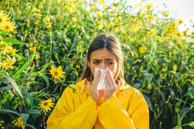 Beautiful sexy young woman lies on flowers background. Young girl sneezing and holding paper tissue in one hand and flower bouquet in other. Flu.