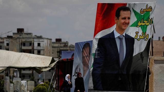 People walk past posters depciting Syria's President Bashar al-Assad, in the district of al-Waer