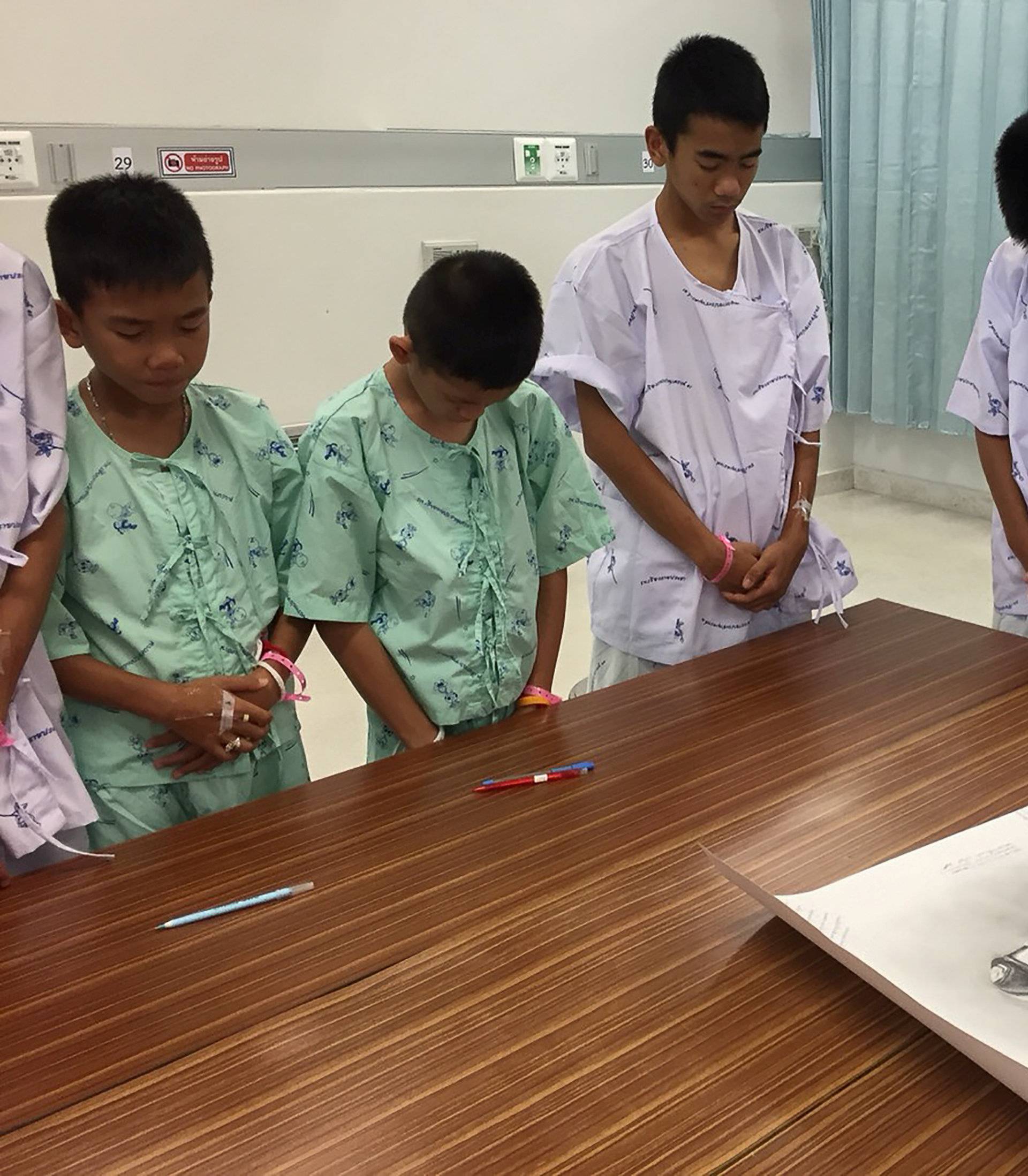 Members of "Wild Boars" soccer team and their coach rescued from a flooded cave bow their heads after writing messages on a drawing picture of Samarn Kunan at the Chiang Rai Prachanukroh Hospital